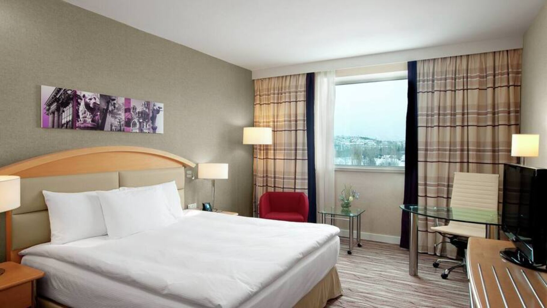 Tan walls, king-size bed with desk area to work and corner window view.