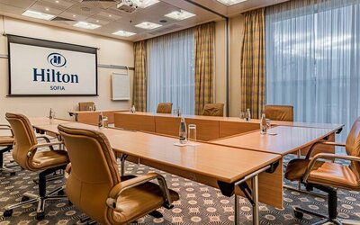 Long u-shaped light brown wooden table with seating for 8-10 guests.