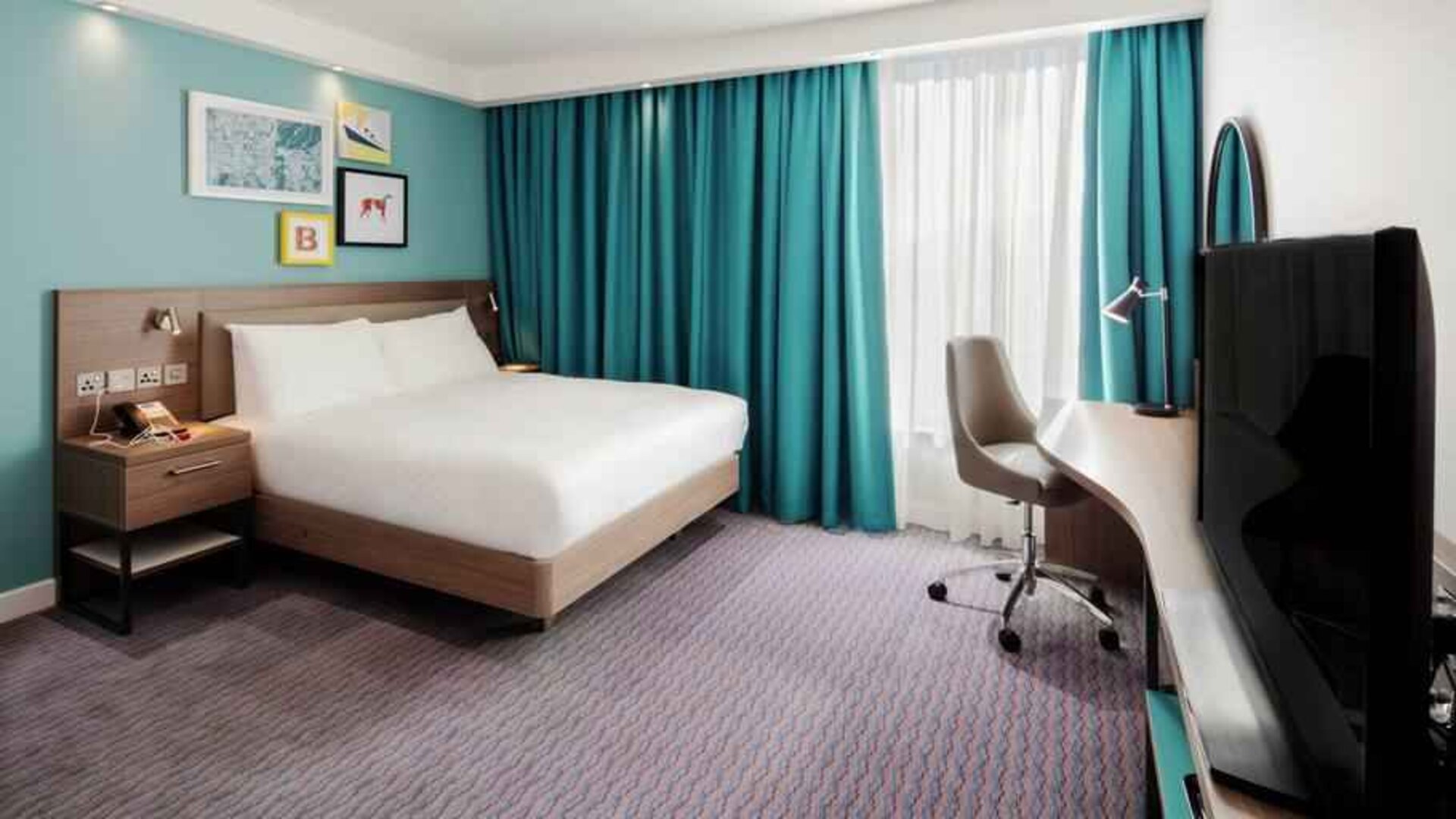King guestroom with TV screen and desk at the Hampton by Hilton Belfast City Centre.