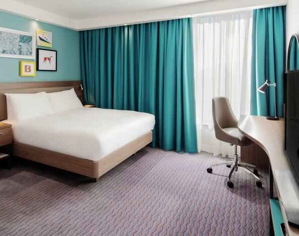 King guestroom with TV screen and desk at the Hampton by Hilton Belfast City Centre.