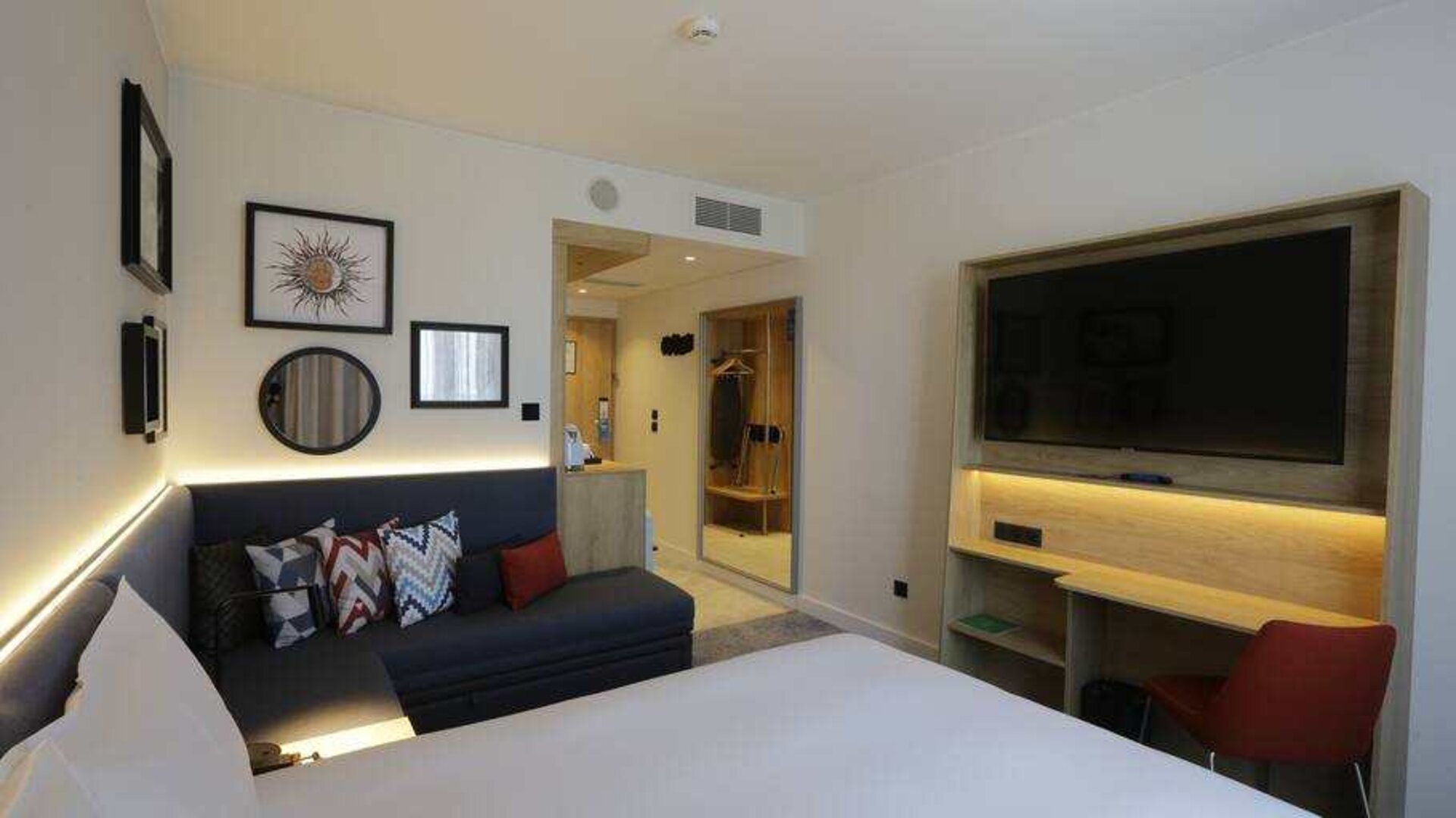 Hotel room with sofa, desk and TV screen at the Hampton by Hilton Olsztyn.