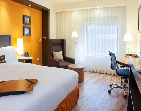 comfortable delux king room with TV, desk, chair, and couch at Hampton by Hilton Vadodara-Alkapuri.
