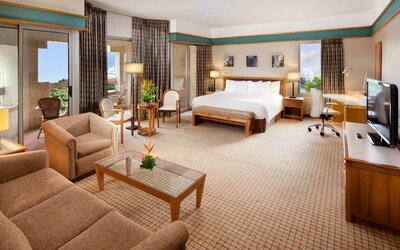 Spacious king suite with king bed, city view, sliding doors, desk, chairs, media console and tv, and sofabed at the Hilton Yaounde.