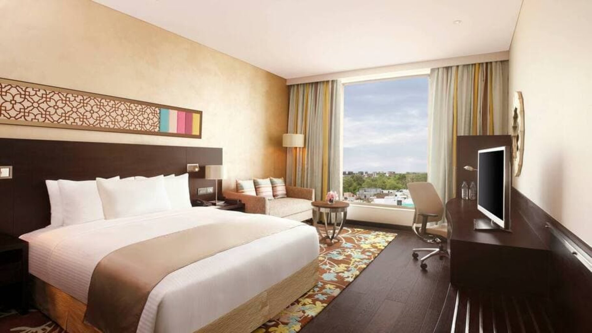 Spacious executive day room with floor-to-ceiling window, large desk, television, king bed at the Hilton Jaipur.