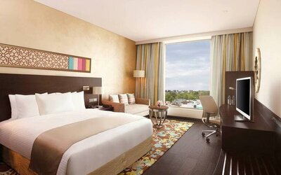 Spacious executive day room with floor-to-ceiling window, large desk, television, king bed at the Hilton Jaipur.