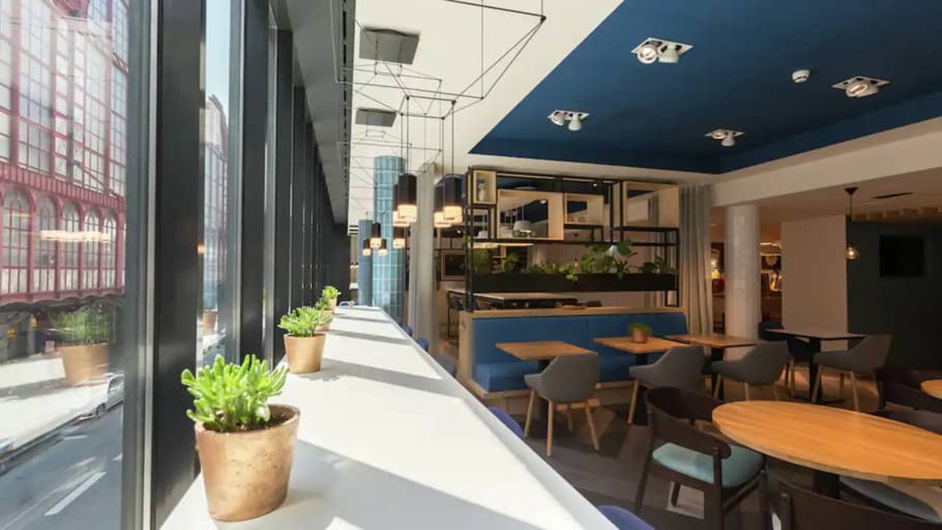 White sunlit table lines window with succulents, other small tables for 1-2 people fill a spacious lobby, perfect for working remotely.