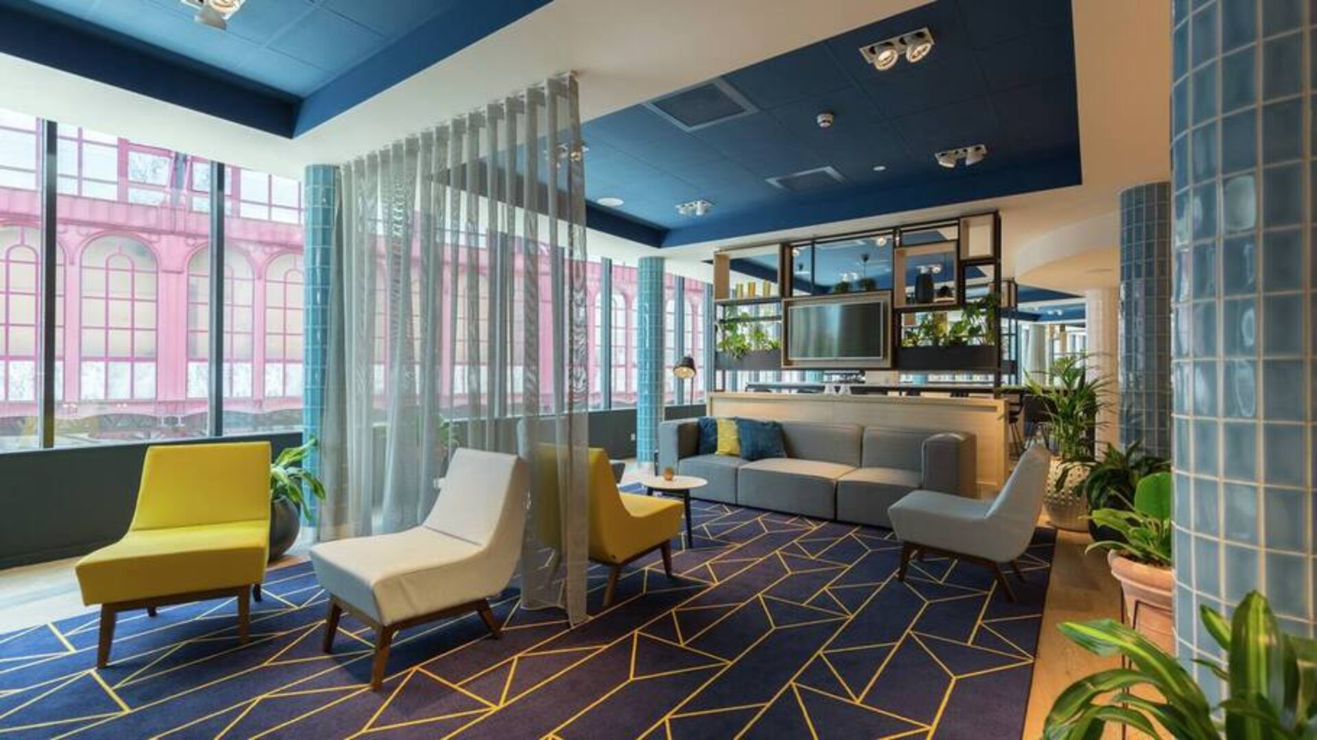 Stylish muted gold and pale blue lounge chairs along with a couch complement a blue and white geometric rug in the Antwerp Hilton lobby.