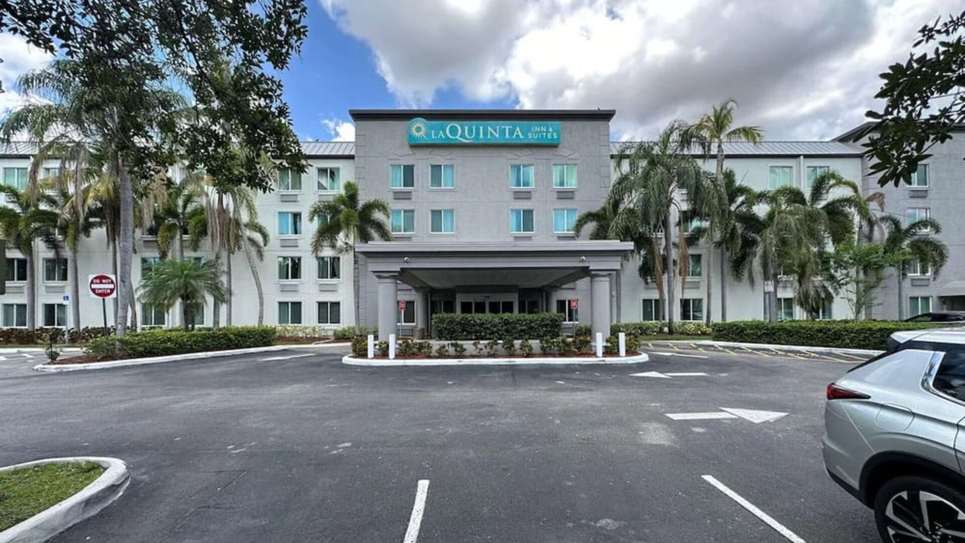 Exterior view of the hotel showcasing the main entrance, palm-lined surroundings, and convenient on-site parking at La Quinta Inn & Suites By Wyndham Sawgrass Mills.