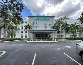 Exterior view of the hotel showcasing the main entrance, palm-lined surroundings, and convenient on-site parking at La Quinta Inn & Suites By Wyndham Sawgrass Mills.