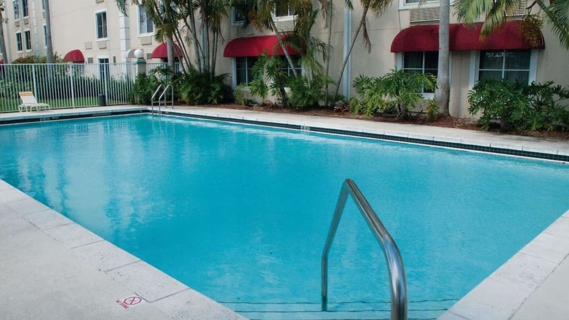 Outdoor pool area surrounded by tropical landscaping, creating a refreshing setting for relaxation and leisure at La Quinta Inn & Suites By Wyndham Sawgrass Mills.