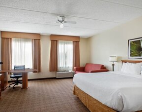 Large guest room featuring a king-size bed, separate seating area, work desk, and ample floor space, providing comfort and convenience for both short and extended stays at La Quinta Inn & Suites By Wyndham Sawgrass Mills.