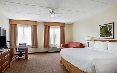 Large guest room featuring a king-size bed, separate seating area, work desk, and ample floor space, providing comfort and convenience for both short and extended stays at La Quinta Inn & Suites By Wyndham Sawgrass Mills.