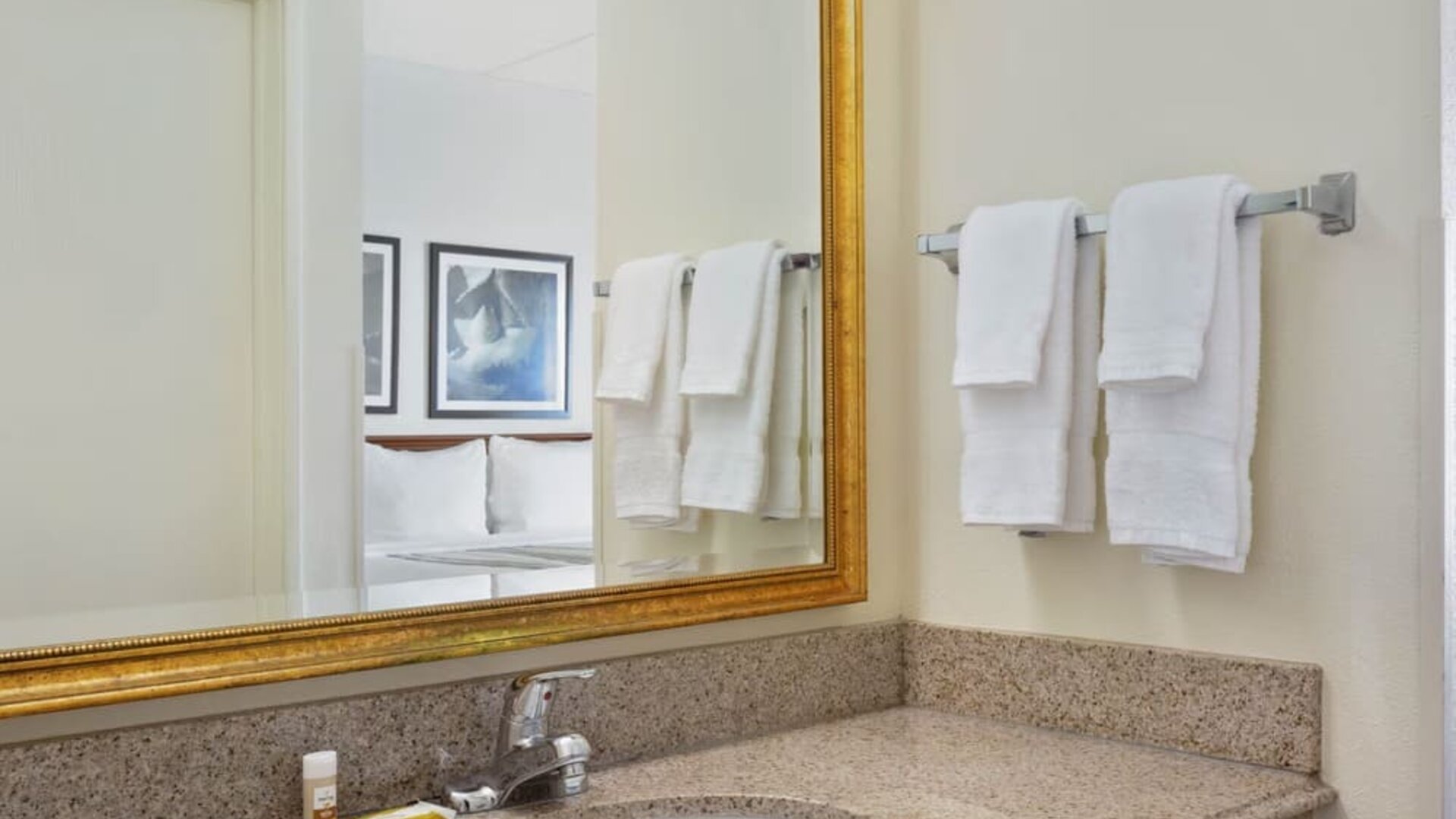 Bathroom vanity area featuring a granite countertop, large framed mirror, fresh towels, and complimentary toiletries, providing guests with a convenient and comfortable space to prepare for the day.