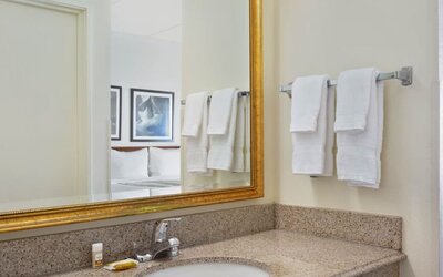 Bathroom vanity area featuring a granite countertop, large framed mirror, fresh towels, and complimentary toiletries, providing guests with a convenient and comfortable space to prepare for the day.