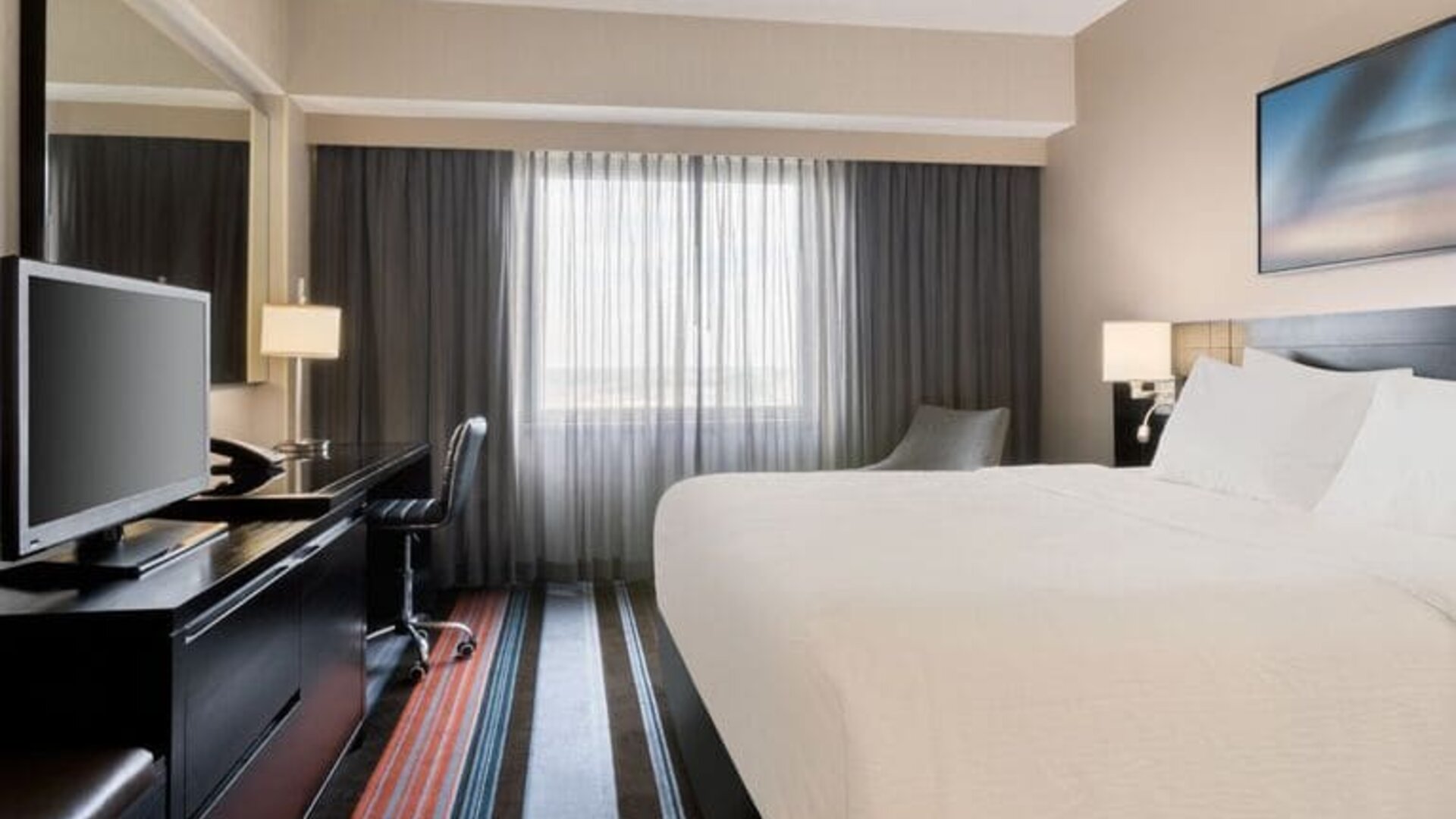 Spacious delux king room with TV, business desk, and couch at Courtyard By Marriott New York JFK Airport.