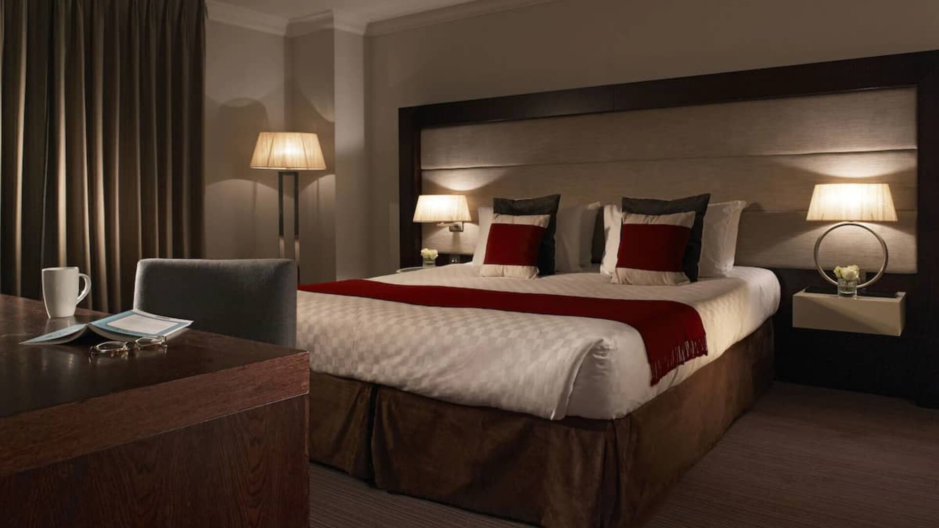 Calm lighting, king size bed with sunlight coming through the shades and reflecting on the workspace, at the Thistle Holborn in London.