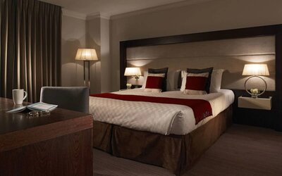 Calm lighting, king size bed with sunlight coming through the shades and reflecting on the workspace, at the Thistle Holborn in London.