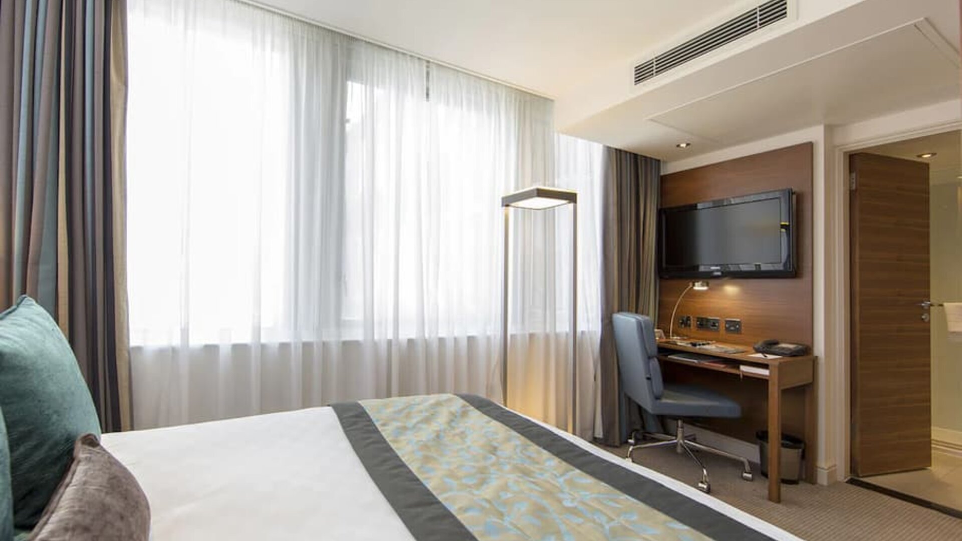 Brightly lit room with king bed and workspace with wall-mounted flat screen TV above.