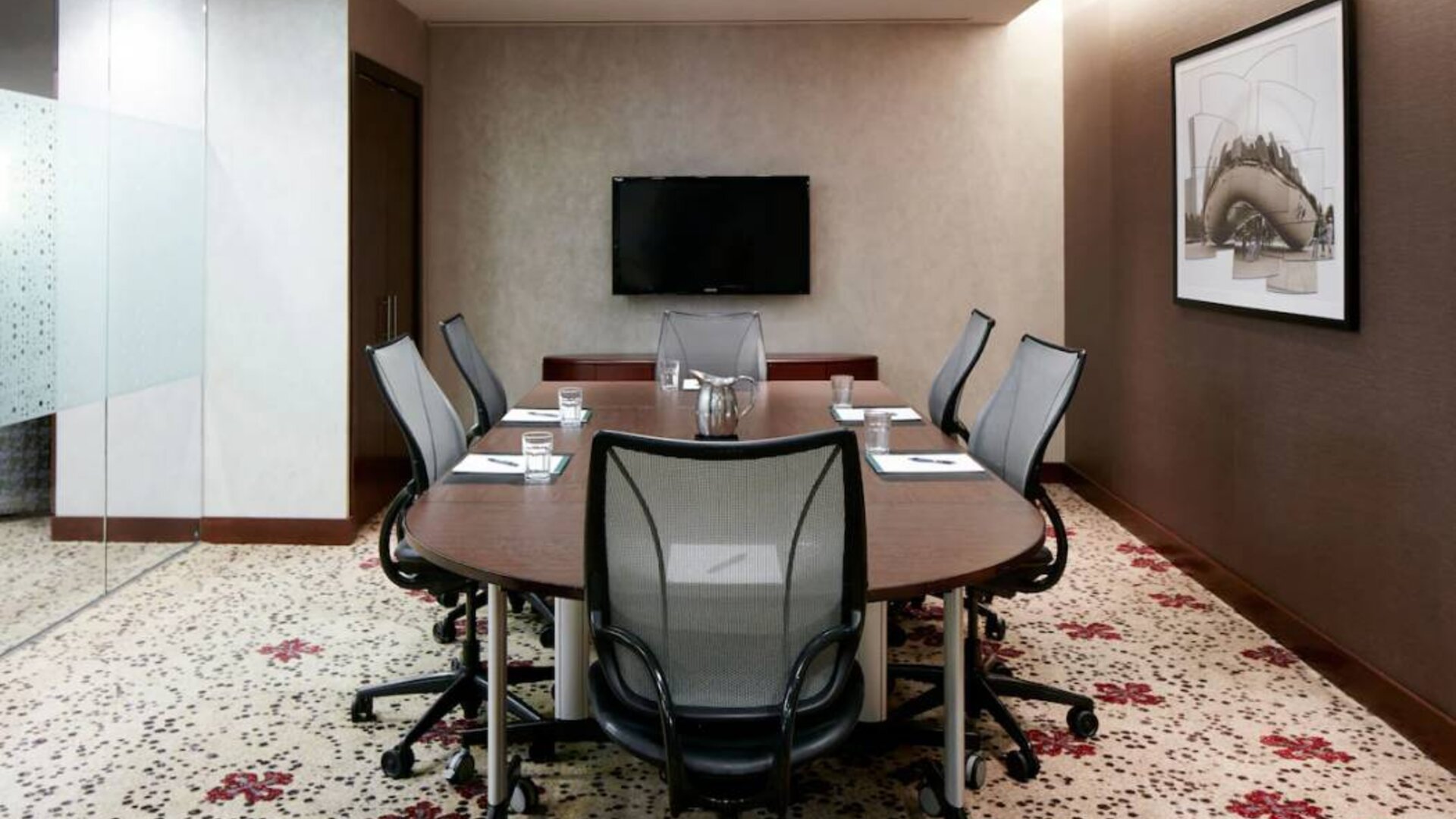 Meeting room in the hotel, with art and TV on the walls and half a dozen chairs arranged around a long table.
