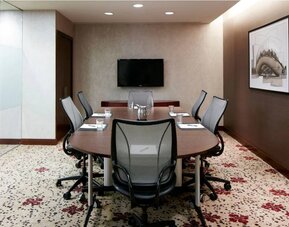 Meeting room in the hotel, with art and TV on the walls and half a dozen chairs arranged around a long table.