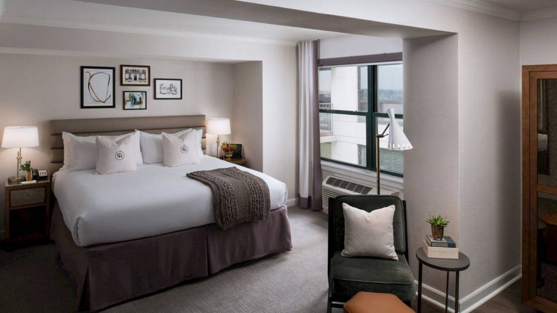 Double bed guest room in Claridge House, with art on the wall, window, and comfortable chair, footstool, and coffee table.