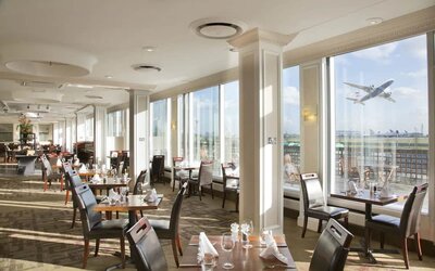 Sunlight room with floor to ceiling windows spanning the entire length of the wall to see planes takeoff and land at London Heathrow Airport.