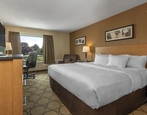 Queen size bed, dresser with television. Work desk next to large window with view of trees.