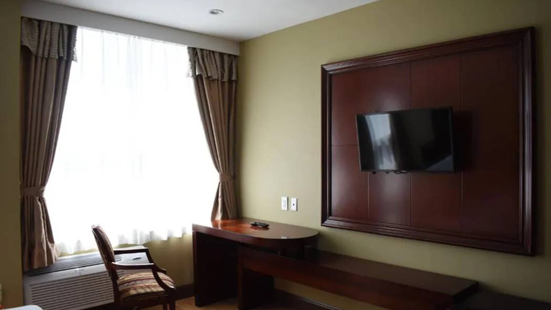 A Queens Hotel guest room with chair and table for working, and a nearby window.