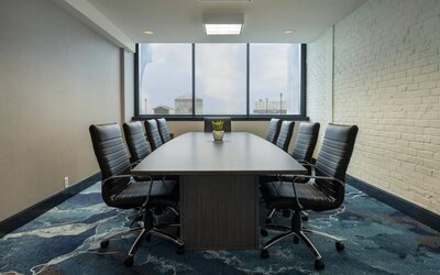 Hotel meeting room with a long wooden table and surrounding leather chairs.
