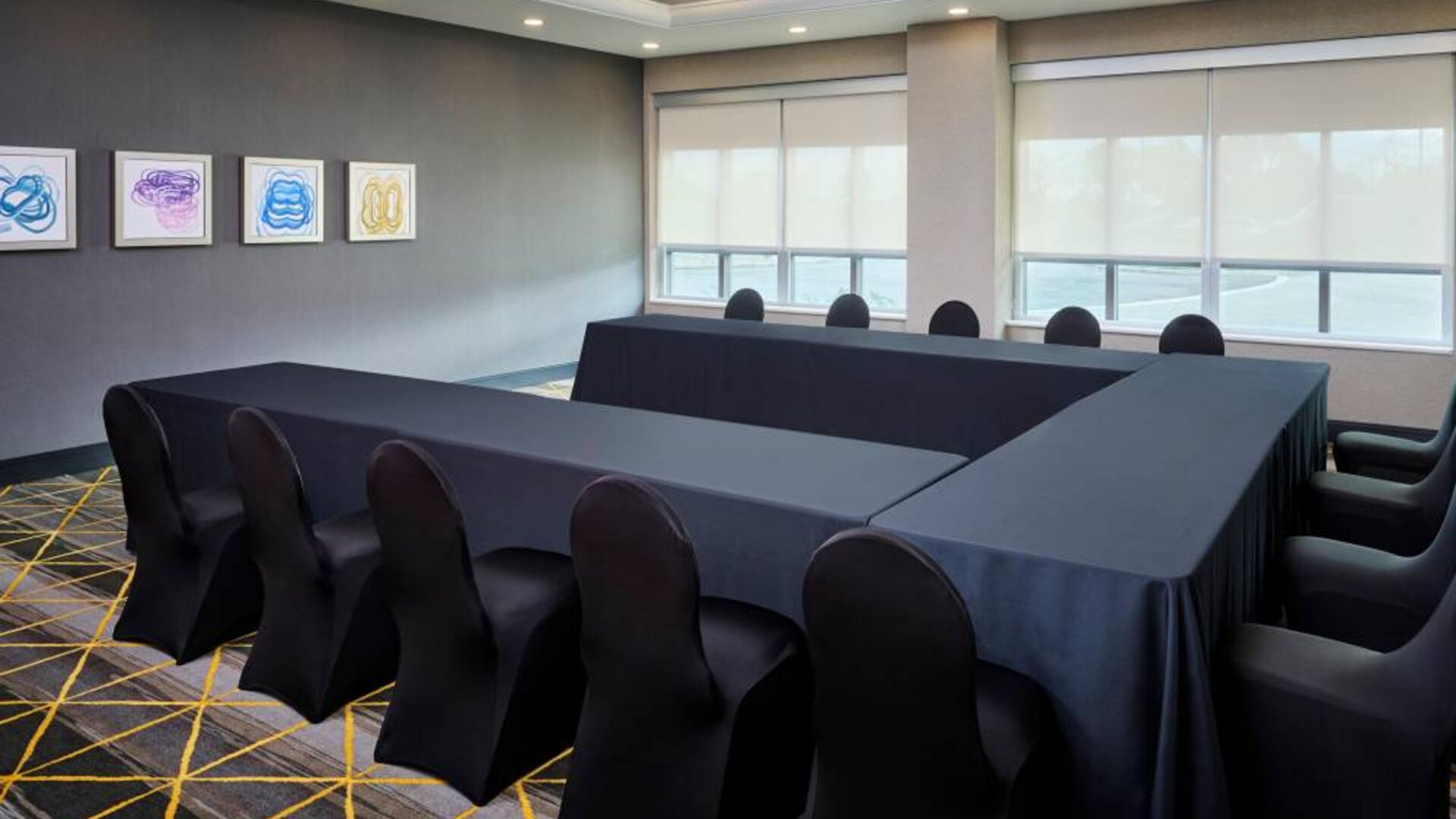 Hotel meeting room with three tables arranged in a U-shape and seating for over a dozen attendees.