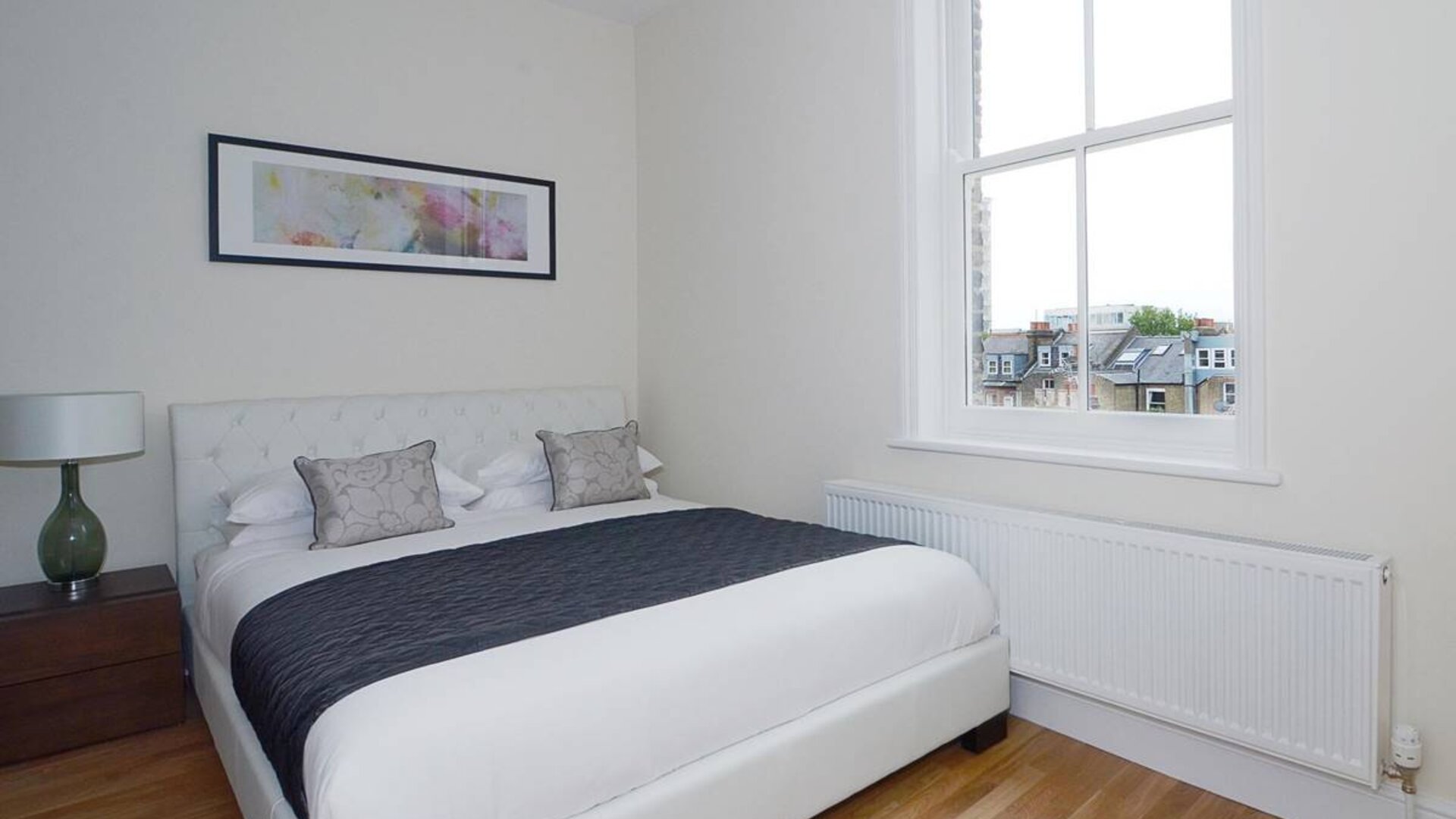 Hammersmith One’s bedroom, with double bed, bedside lamp, and nearby window.