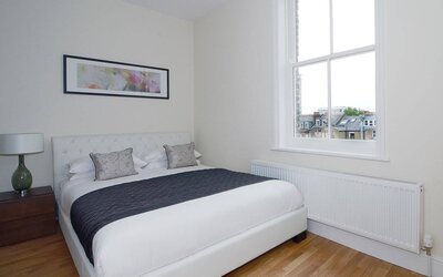 Hammersmith One’s bedroom, with double bed, bedside lamp, and nearby window.