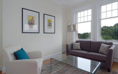 Living room with armchair, sofa, windows, and glass table.