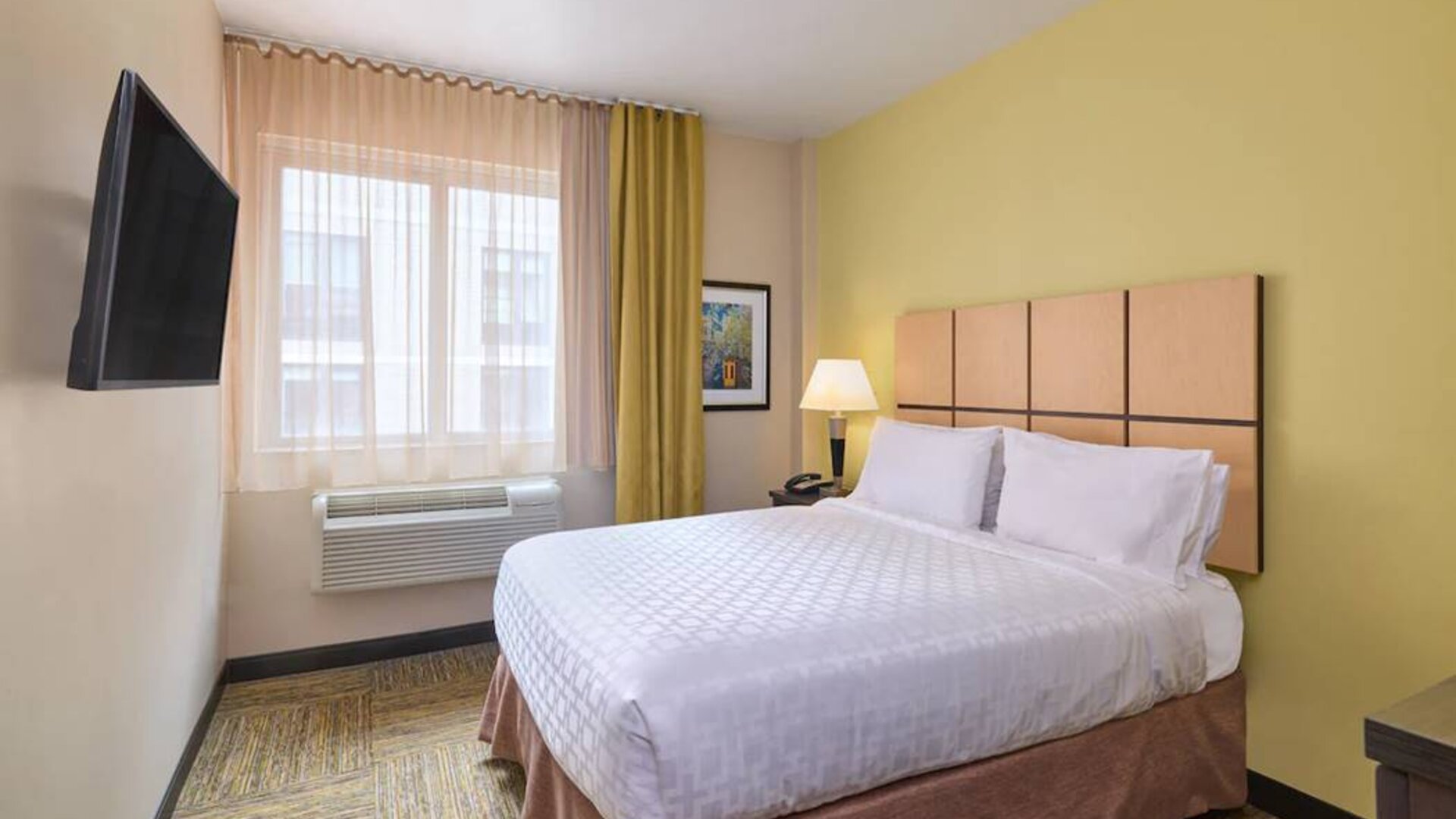 A guest room in the Candlewood Suites Times Square, with double bed, large TV, and window.