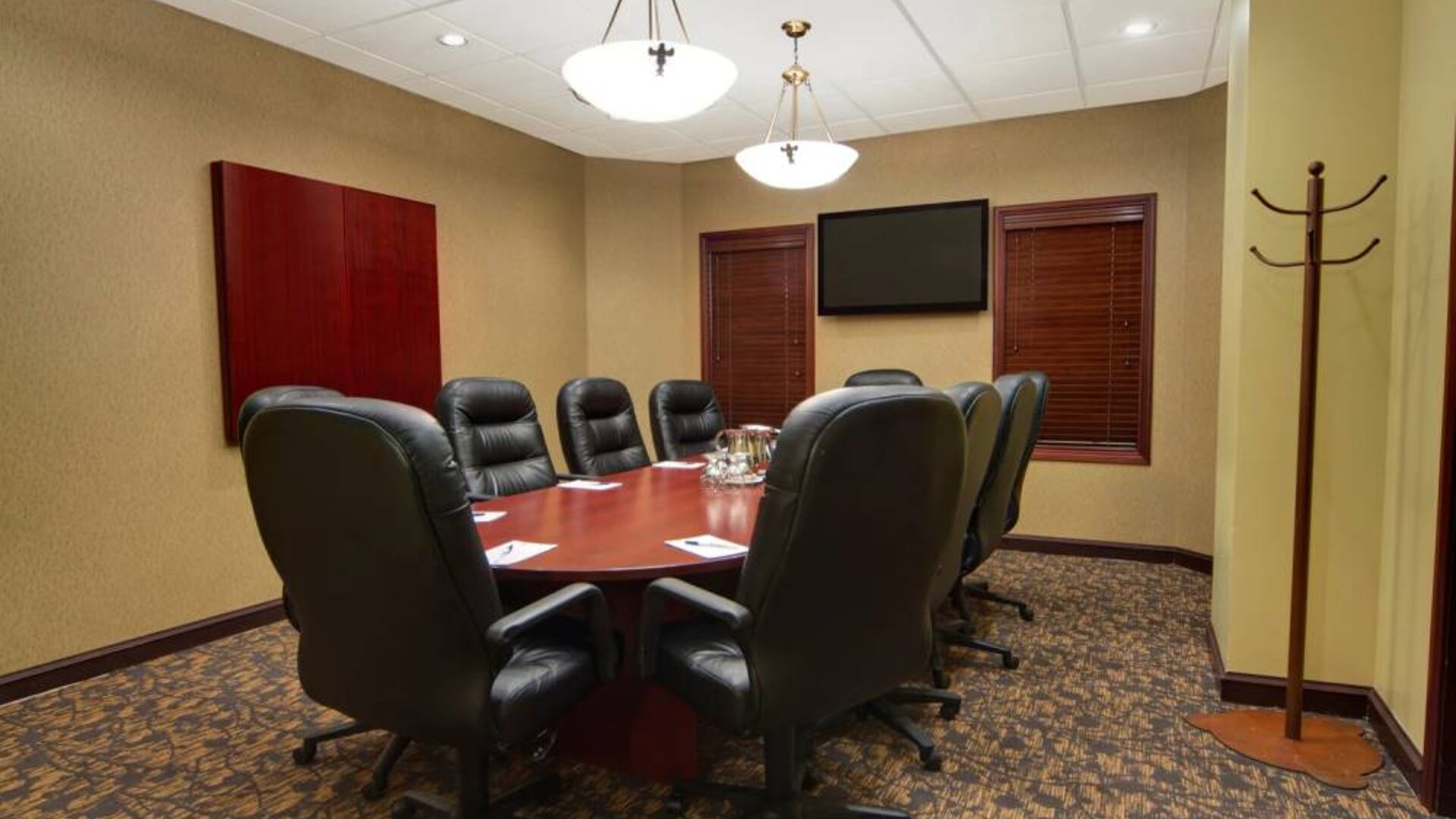 Hotel meeting room with long wooden table, plush leather swivel chairs, and widescreen TV.