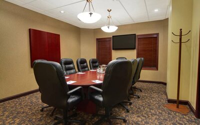 Hotel meeting room with long wooden table, plush leather swivel chairs, and widescreen TV.