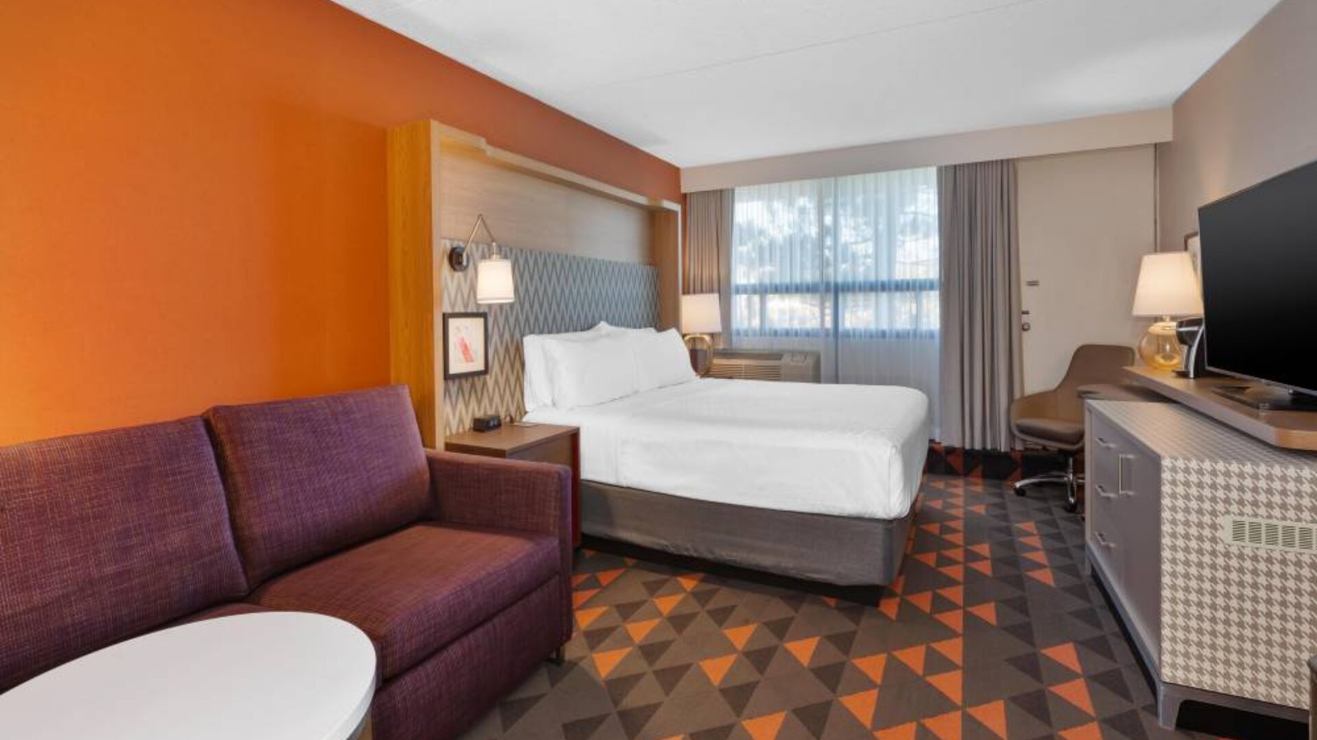 Guest room in Holiday Inn St. John’s Conference Centre, with large double bed and window, plus sofa and TV.