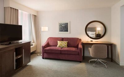 The Hampton Inn Times Square South’s king mobility suite lounge, with desk, sofa, and television.