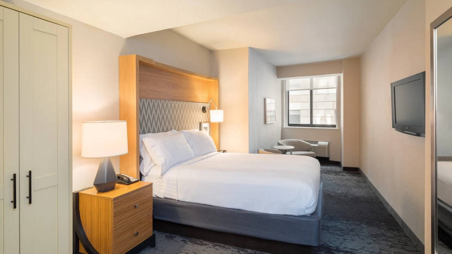 Guest room in the Holiday Inn Express Wall Street, with large television, chairs, and window.