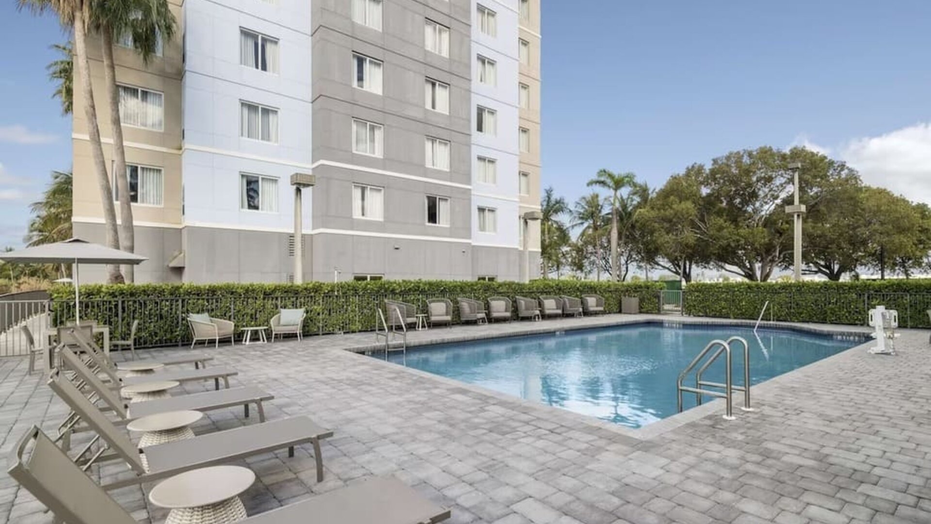 Loungers beside outdoor pool at Homewood Suites By Hilton Miami Airport-Blue Lagoon.
