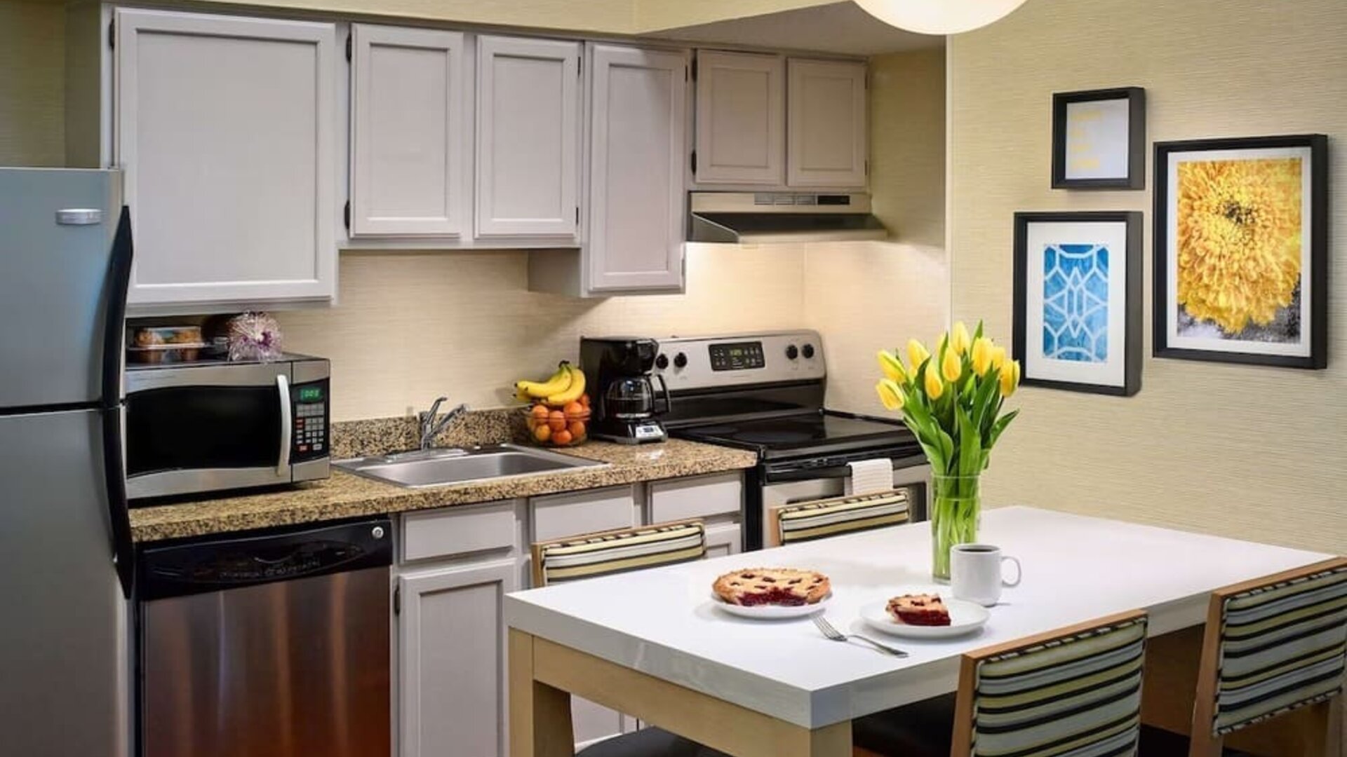 Sonesta ES Suites Tucson guest room kitchen area, equipped with hob, oven, microwave, sink, and fridge freezer, plus dining table.