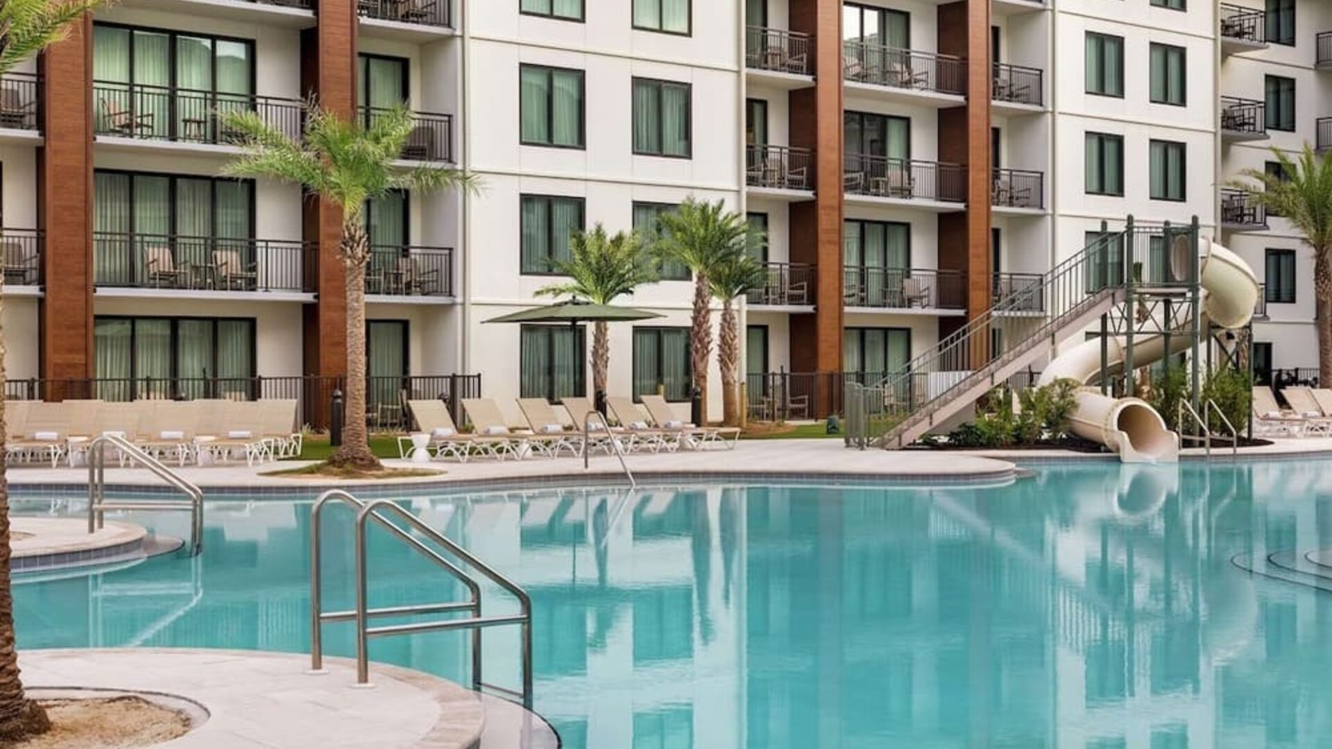 Outdoor pool with water slide and lounge chairs at Embassy Suites By Hilton Panama City Beach Resort.