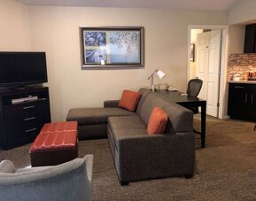 Sonesta ES Suites San Jose Airport guest room lounge with TV, sofa, and armchair, with adjacent workspace area.