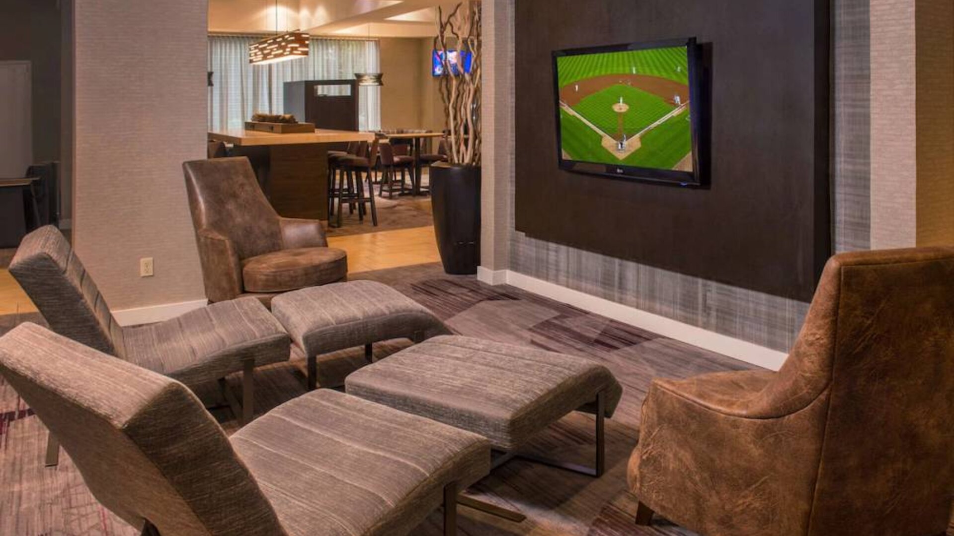 Sonesta Select Arlington Rosslyn’s lobby features a large, wall-mounted TV, with armchairs and reclined seating with footstools.