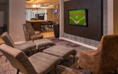 Sonesta Select Arlington Rosslyn’s lobby features a large, wall-mounted TV, with armchairs and reclined seating with footstools.