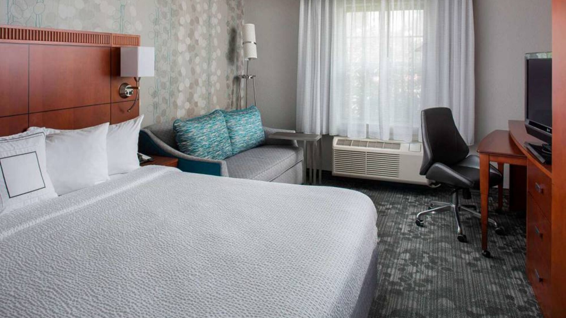 Sonesta Select Boston Lowell Chelmsford double bed guest room, featuring sofa, TV, and workspace desk and chair.