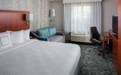 Sonesta Select Boston Lowell Chelmsford double bed guest room, featuring sofa, TV, and workspace desk and chair.