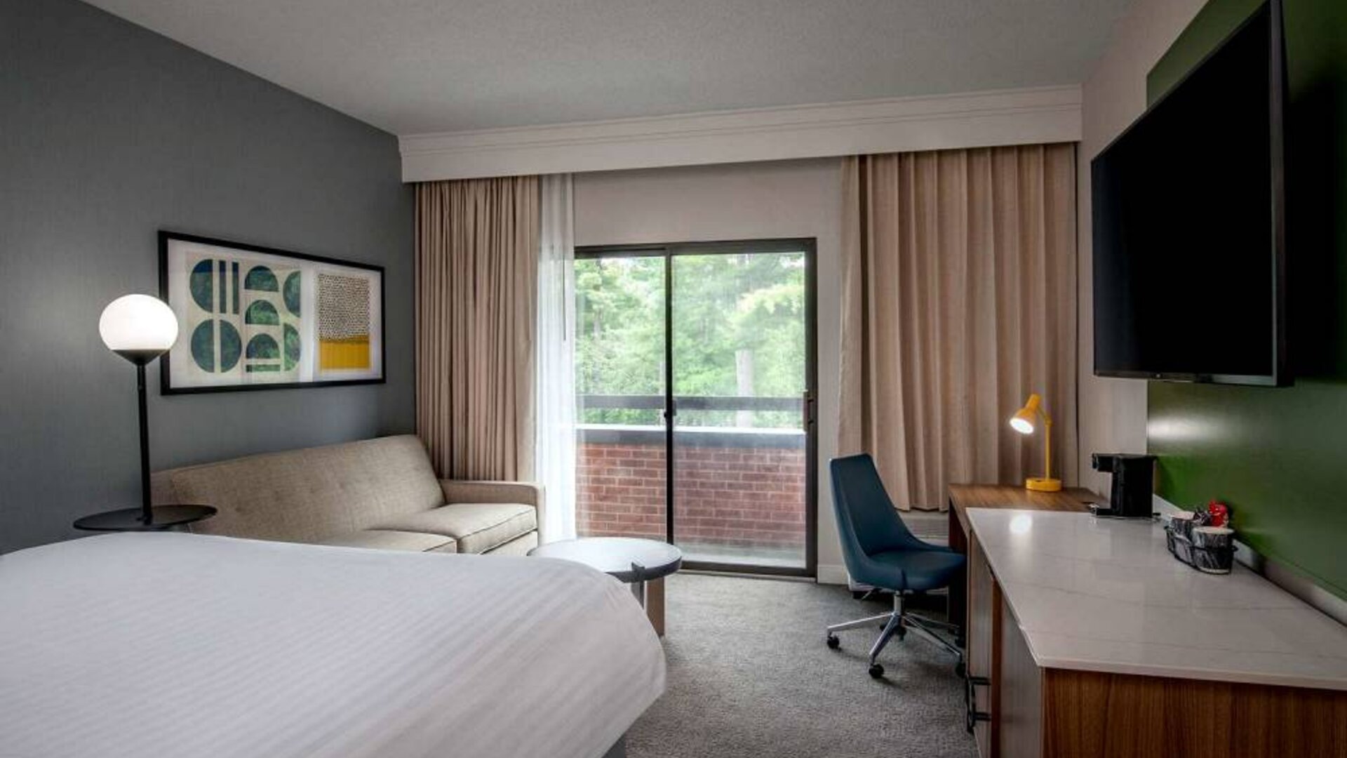 Sonesta Select Boston Foxborough Mansfield double bed guest room, featuring sofa, TV, and workspace desk and chair.