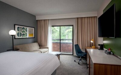 Sonesta Select Boston Foxborough Mansfield double bed guest room, featuring sofa, TV, and workspace desk and chair.