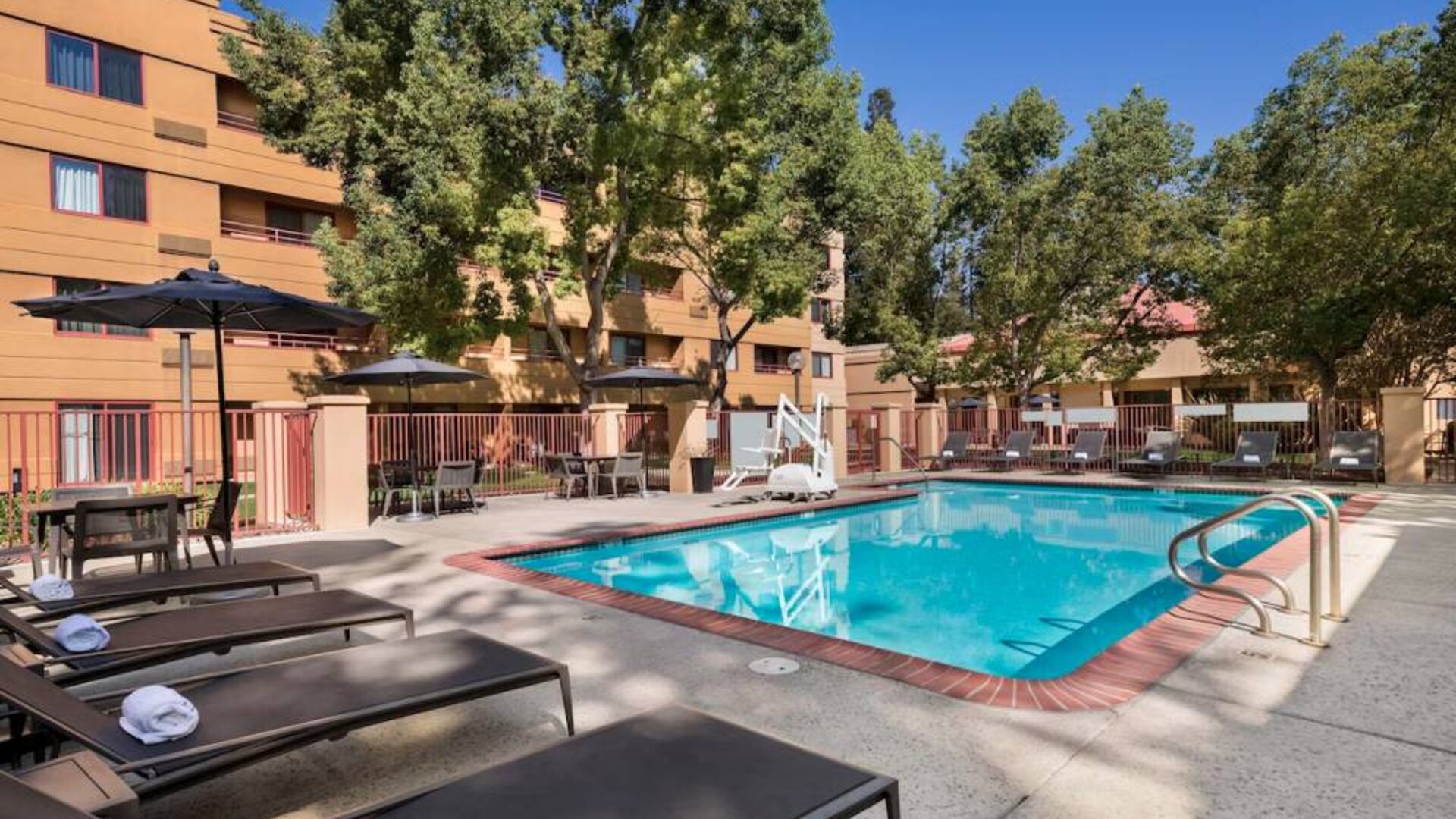 The outdoor pool at Sonesta Select San Jose Airport features a lift, and has nearby sun loungers and shaded tables and chairs.